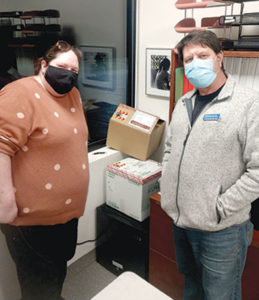 Louis Kuchnir, MD stands with his office manager, Jane, and his shipment of COVID-19 vaccines in elaborate cardboard boxes. He opened a COVID-19 vaccine clinic.