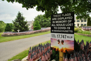 A sign notes the number of deaths due to COVID-19 in Massachusetts as marked by flags on the property of Grafton’s Mike Labee. 