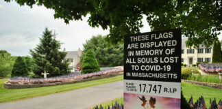 A sign notes the number of deaths due to COVID-19 in Massachusetts as marked by flags on the property of Grafton’s Mike Labee.