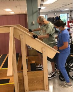 Ralph practices climbing stairs during his rehabilitation program as a staff member assists. 