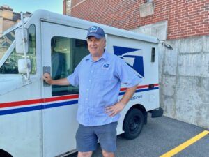 Marlborough mailman Chad Wiggin standing beside postal delivery truck, Postmaster General Hero Award recipient