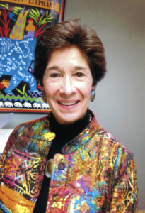 Linda LeSage, author, smiling portrait with colorful artwork in background