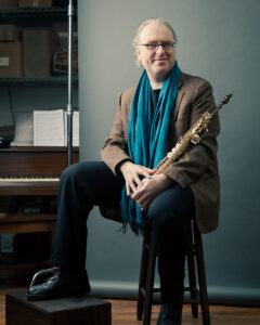 Russ Gershon, founder of the Either/Orchestra, wearing a blue scarf and holding a saxophone.