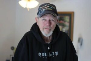 Andy Kjellberg, veteran from Grafton, wearing a black hoodie and military cap, standing indoors with a focused expression, symbolizing dedication to honoring fellow veterans.