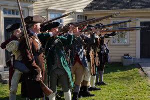 Colonial reenactors in period attire aiming muskets, representing the Battle of Menotomy during Patriots' Day celebrations in Arlington, Massachusetts.