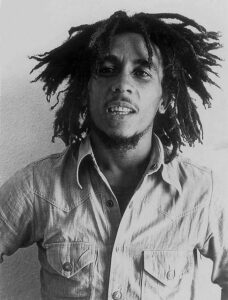 Bob Marley in a denim shirt with dreadlocks, symbolizing the reggae music scene that influenced Boston college students in the 1970s.