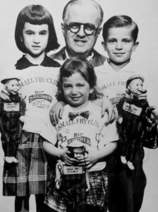 Big Brother Bob Emery with three children, all wearing "Small Fry Club" shirts, holding dolls, promoting engagement and education in children's television.