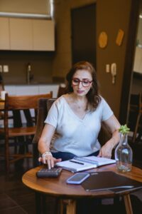 Woman calculating retirement savings at a table with a notebook, calculator, and smartphone, reflecting financial planning in Massachusetts.