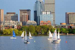 Sailboats on the Charles River with Boston skyline in the background, showcasing a vibrant spring day ideal for luxury staycations.