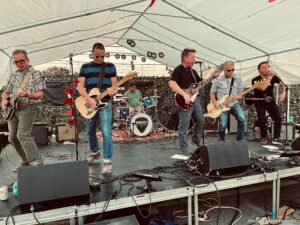 The Dogmatics band performing live rock music under a white tent.